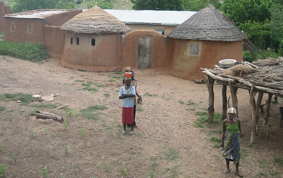 People walking in front of houses in Togo. Erik Kristensen, CC BY 2.0 , via Wikimedia Commons