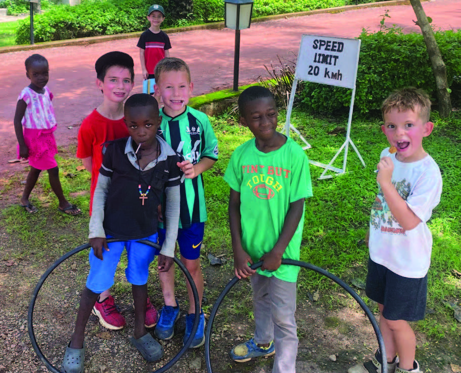 A group of children striking playful poses on a grassy terrain, some joyfully holding hula hoops