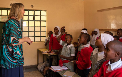 A teacher standing in front of students seated at desks in a classroom, engaging with them during a lesson.