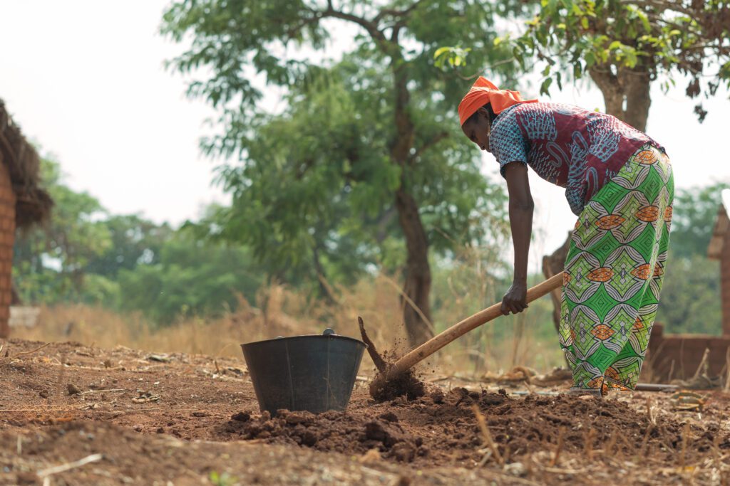 Fulani woman digging in dirt with pick in West Africa | SIM International